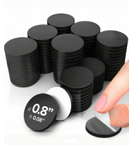 A pack of black circular magnetic discs stacked in groups, with one disc shown in the foreground displaying printed dimensions and a hand peeling off a transparent protective cover from another disc.