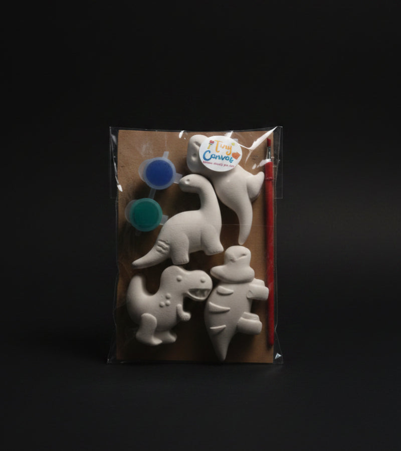 A packaged children's dinosaur painting kit. The kit includes four unpainted white dinosaur shapes, two small paint pots, a paintbrush.