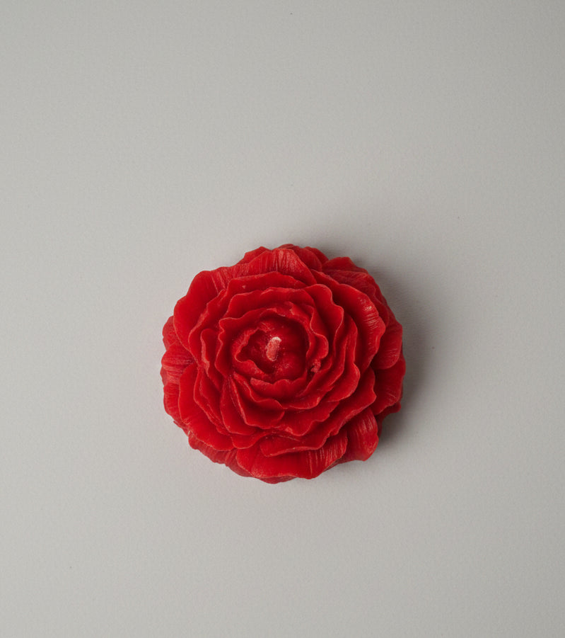 A red rose flower candle shown flat against a light gray textured background.