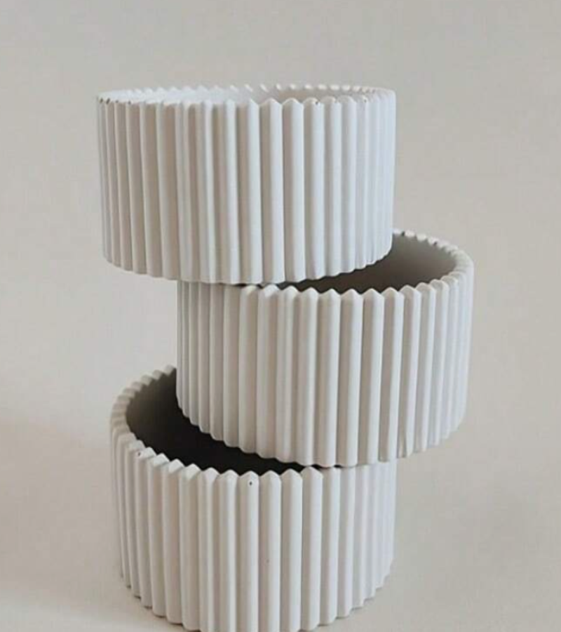 Three white ribbed ceramic containers stacked on a light beige background.