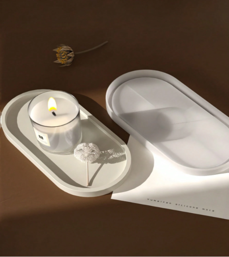 A minimalist white oval tray placed on a dark brown surface next to silicone tray mold.
