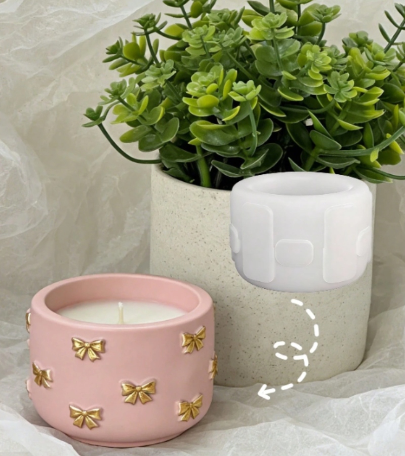 A pink ceramic candle holder with gold bow details in the foreground, next to a silicone mold