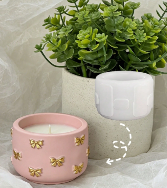 A pink ceramic candle holder with gold bow details in the foreground, next to a silicone mold
