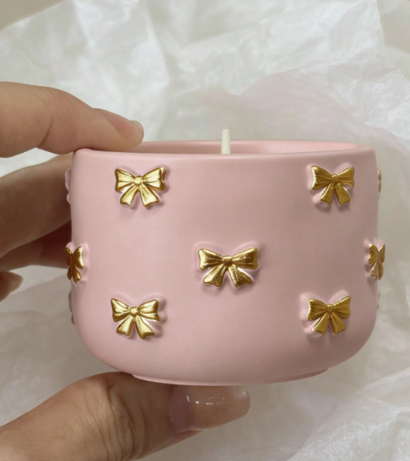 A pink ceramic candle holder with raised gold bow details
