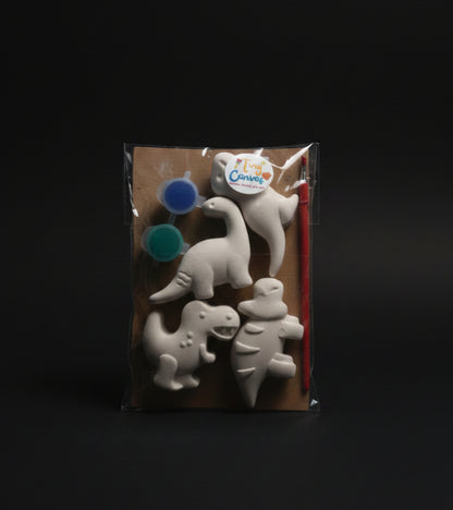 A packaged children's dinosaur painting kit. The kit includes four unpainted white dinosaur shapes, two small paint pots, a paintbrush.