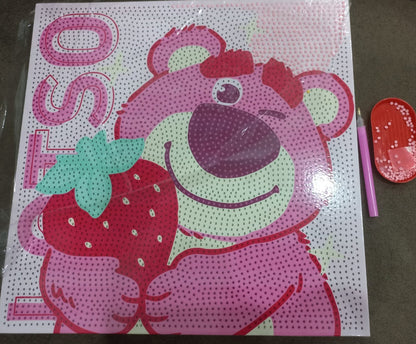 A square diamond painting or dot art kit featuring a pink cartoon bear holding a red strawberry, with the word 'LOTSO' on the left. The kit is shown on a dark surface next to a pink tool and a red oval accessory.