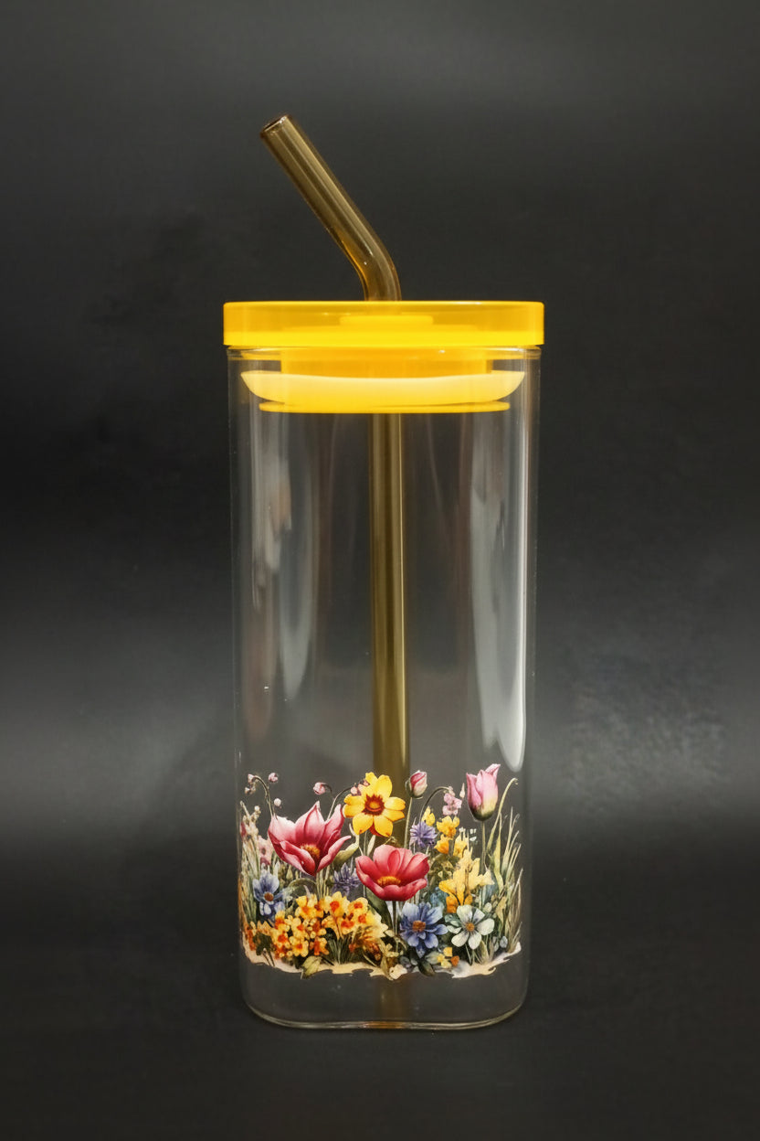 A clear plastic tumbler with a yellow lid and a colorful floral print near the bottom, containing a yellow straw, set against a dark background.