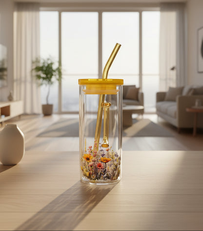 A clear glass tumbler with a yellow lid and straw, decorated with a colorful wildflower pattern near the bottom, shown against a dark background.